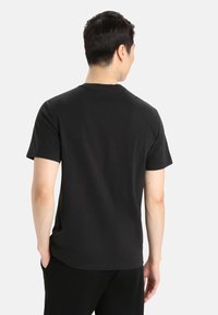 Black crew-neck t-shirt made of cotton, short sleeves, with a smooth texture. Displayed from the back, tucked into black pants.