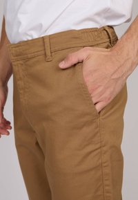 Pantalon en coton brun doté de passants de ceinture, de poches latérales et d'une texture lisse, mettant en valeur un design classique à jambe droite.