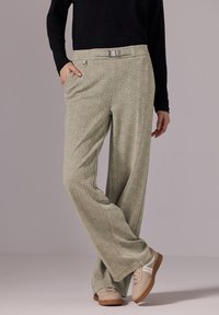 Pantalones verdes claros de patrón con un corte relajado, que presentan un cinturón, bolsillos laterales y una textura suave. Llevados con zapatillas de deporte beige claro.