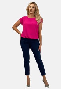 Fuksjowa bluzka z krótkim rękawem w połączeniu z granatowymi dopasowanymi spodniami. Modelka nosi szpilki w wężowy print. Gładka tekstura, casualowy styl i dopasowany krój.