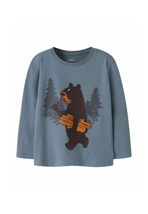 Chemise bleue à manches longues pour enfants avec un ours de dessin animé portant des bûches et faisant signe, sur fond de silhouettes d'arbres sombres.
