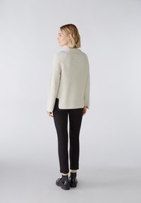 Hellgrauer, ribbeliger Pullover mit lockerer Passform, seitlichen Schlitzen und langen Ärmeln, kombiniert mit schwarzen Slim-Fit-Hosen und klobigen schwarzen Schuhen.