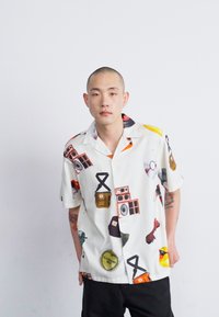 Camisa de manga corta en tela blanca con gráficos impresos coloridos de equipos de audio retro y otros motivos. Cuello abotonado, corte relajado.