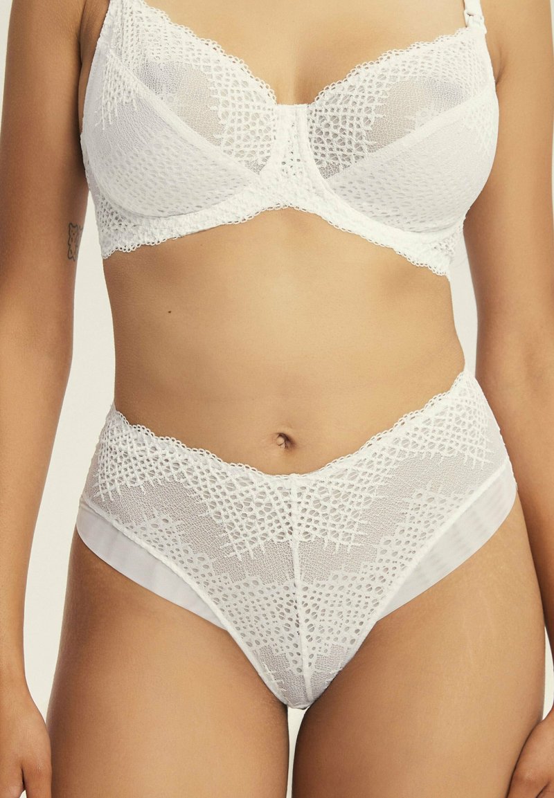 Weißes Spitzen-BH- und hochgeschnittenes Unterhosen-Set mit strukturierten Mustern, floralem Design und Satinelementen an den Seiten.