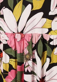 Tissu floral audacieux avec de grandes fleurs blanches, roses et orange et des feuilles vertes et jaunes sur fond noir, avec un détail de couture froncée.