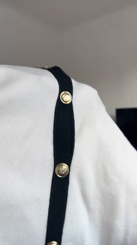 Balts ribots audums topiņš ar melnu samta apmalīti. Zelta tonī pogas gar apmalīti piešķir detaļas. Dizainam ir klasiska, eleganta izskats.