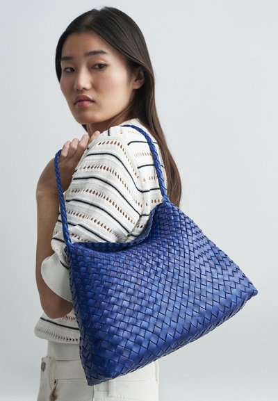 Ύφασμα από δέρμα υφασμένο tote τσάντα σε ζωντανό μπλε, με χαλαρή σιλουέτα, πλεχτές λαβές και υφασματική επιφάνεια.