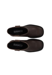 Botas de cuero marrón hasta el tobillo con punteras cuadradas, dos asas en los costados y suelas de goma negra. La marca aparece en la plantilla.