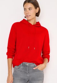 Felpa rossa con cappuccio regolabile e polsini a costine, caratterizzata da una vestibilità comoda. Abbinata a jeans grigi, il colore vivace contrasta con l'abbigliamento casual.