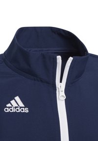 Marine windbreaker jacket met een hoge kraag, witte rits en geborduurd logo. De textuur lijkt glad met gestikte details.