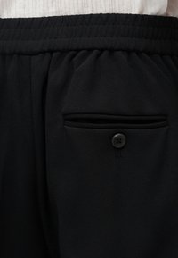 Μαύρο παντελόνι με ελαστική μέση, κουμπωτή πίσω τσέπη και ορατή ραφή στη μέση.