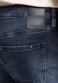 Donkerblauwe denim jeans met een gestructureerd oppervlak. Kenmerken zijn een zwart leren label met "NO EXCESS" en een zijzak met een klein etiket.
