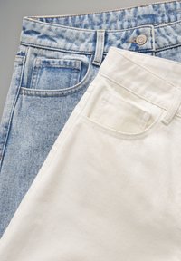 Vaqueros de mezclilla azul claro con acabado desgastado y pantalones de algodón blanco. Ambos cuentan con bolsillos y cierres estándar de botón.