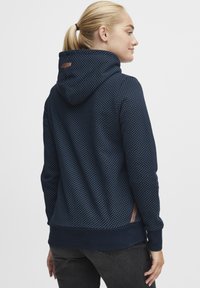 Hoodie bleu marine avec un motif à pois, capuche avec cordon de serrage et cuffs côtelés. Présente un accent en cuir avec logo sur le côté. Tissu texturé.
