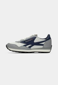 Muške atletske cipele u bijeloj i mornarsko plavoj boji s akcentima od antilopa i mrežaste tkanine, klasičan dizajn za trčanje, teksturirana siva potplat i vezice. Prikazan Reebok logo.