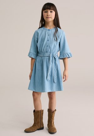 Svetlo modra jeansa obleka s kratkimi rokavi, spredaj z gumbi, z volančki, zategnjena v pasu s pentljo. Oblečena s rjavimi semiš škornji, ki spominjajo na kavbojske čevlje.