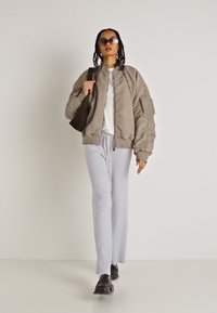 Casaco bomber cinza claro com textura canelada, camiseta branca e calças largas cinza claro. Sapatos pretos e óculos de sol oversized completam o visual.