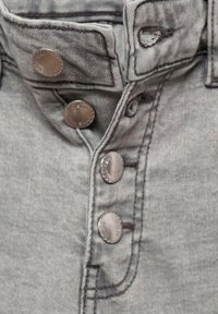Sivkasta denim blago s zapiranjem na gumb. Ima kovinske gumbe in potrebne šive vzdolž ployke in območja ovratnika.