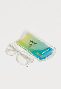Gafas grandes y transparentes con montura dorada, colocadas al lado de un estuche degradado en azul y verde con texto dorado que dice "QUAY."