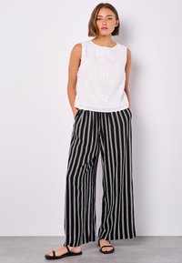 White sleeveless top with floral embroidery, paired with black and white striped wide-leg pants, and black flat sandals.