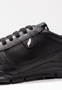 Scarpa in pelle nera con superficie texturizzata, caratterizzata da lacci neri a contrasto e un distintivo dettaglio del logo vicino alla parte superiore. Suola in gomma.
