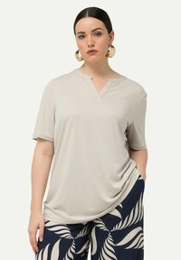 Maglietta corta a maniche con scollo a V in beige chiaro e tessuto morbido, abbinata a pantaloni blu navy a fantasia con motivi di foglie bianche.
