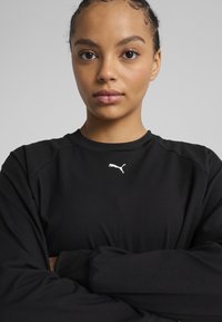 Black long-sleeve shirt with a crew neck and a white Puma logo on the chest. Soft fabric with fitted sleeves and a simple design.