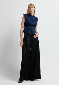 Camisa sin mangas azul marino con una botonera y cintura estructurada, combinada con pantalones largos de satén negros y tacones altos.
