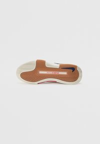 Semelle de chaussure avec une base en caoutchouc au motif en chevrons, beige clair et accents marron, avec une intermédiaire blanche et un logo bleu.