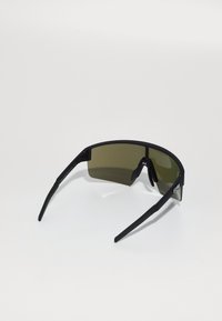 Gafas de sol negras con un armazón ligero, lentes de tono verde y un diseño envolvente. Las características incluyen patillas texturizadas y una bisagra flexible.