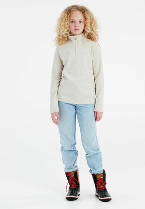 Beiger Fleece-Pullover mit einem Viertel-Reißverschluss, kombiniert mit hellblauen Jeans mit umgeschlagenen Säumen und schwarzen Stiefeln mit roten Akzenten und Kunstfellfutter.