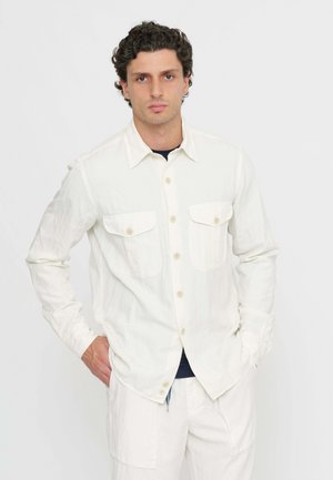 Camicia chiara con bottoni realizzata in tessuto testurizzato, dotata di due tasche sul petto e colletto classico, abbinata a pantaloni chiari.
