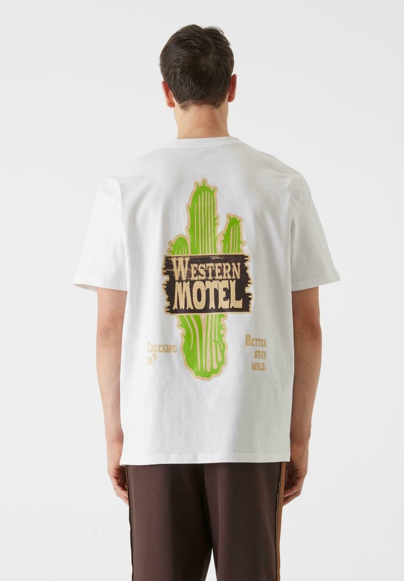 Bijela pamučna majica s grafikom zelenog kaktusa i natpisom "WESTERN MOTEL" u vintage stilu na leđima, s dodatnim frazama ispod.