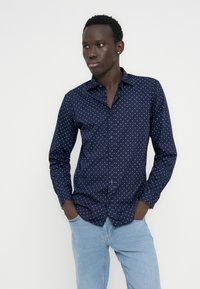 Tumesinine triiksärk valge geomeetrilise mustriga, kitsas lõige, lipsukrae, kombineeritud helesiniste teksadega.