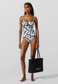 Badedragt i ét stykke med sort-hvidt løvmønster, lav ryg og en nøglehulslomme foran. Suppleret med en struktureret sort tote-taske.