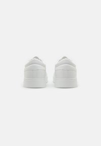 White sneakers with a smooth leather upper, rounded toe, lacing detail, padded collar, and textured rubber sole. Minimalistic design.