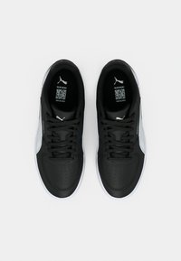 Ζευγάρι ασπρόμαυρα αθλητικά παπούτσια Puma, σε θέαση από ψηλά πάνω σε απλό ανοιχτό φόντο, με εμφανείς την επωνυμία στις πάτους και κωδικούς QR.