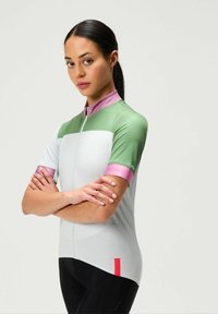 Dámska cyklistická dres s krátkym rukávom v zelenej, bielej a ružovej farbe. Má zapínanie na zips vpredu, športový strih a kontrastné akcenty na rukávoch. Ľahký materiál.
