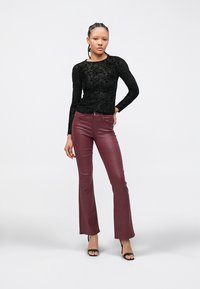 Zwarte top met lange mouwen met bloemrijke kantstructuur en bordeauxrode uitlopende broek met glanzende afwerking. Gecombineerd met zwarte sandalen met hoge hak.