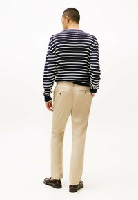 Maglione a righe blu navy e bianche con polsini a coste abbinato a pantaloni beige con tasche posteriori. Modello mostrato di spalle.