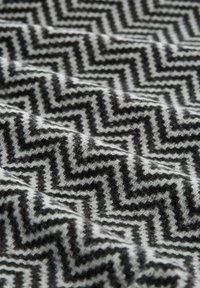 Tela tejida con un patrón de zigzag en tonos de negro y blanco, que presenta una textura suave y un diseño geométrico.