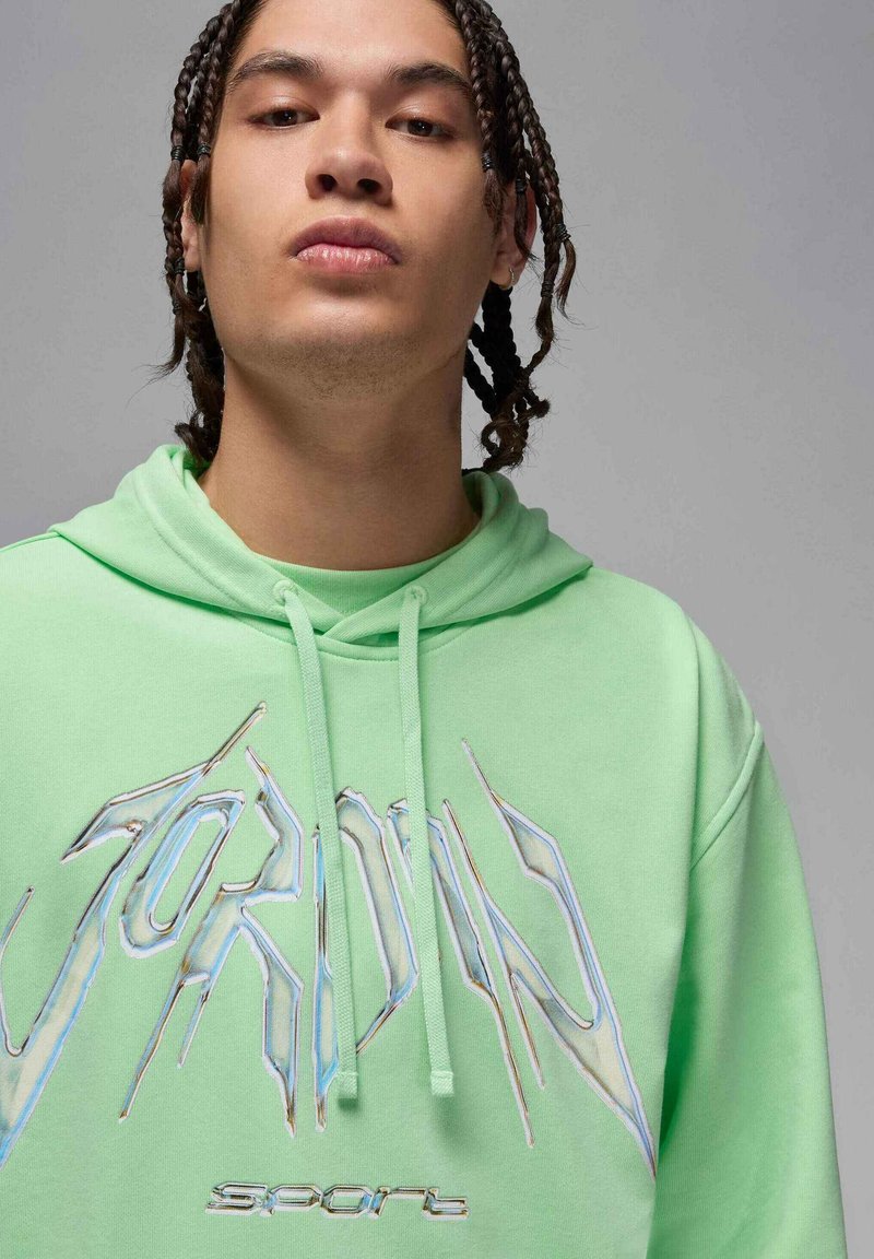 Grüne Kapuzenjacke aus weichem Stoff mit Kapuze, Kordelzügen und großem, stilisiertem "JORDAN"-Logo mit schillernden Akzenten.