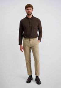 Braunes Langarm-Polohemd mit einer Tasche, kombiniert mit hellbeigen Hosen und dunklen Schuhen. Der Schnitt ist tailliert und modern.