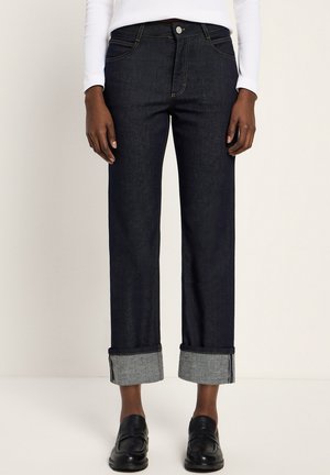 Dark blue denim jeans with a straight fit, rolled cuffs exposing light blue lining, five-pocket design, and gold stitching. Black shoes worn.