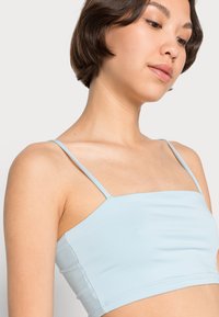 Top cropped azul claro feito de um tecido suave com finas alças ajustáveis, apresentando um decote quadrado e design justo.