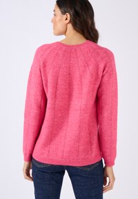 Maglione rosa in lana con maniche lunghe, scollatura rotonda e cuciture verticali testurizzate. Il maglione ha una finitura morbida e pelosa e un orlo a coste.