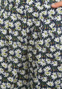 Tela con densas flores de margarita blanca y pequeños acentos florales en naranja y azul sobre un fondo azul oscuro, sostenida por una mano.