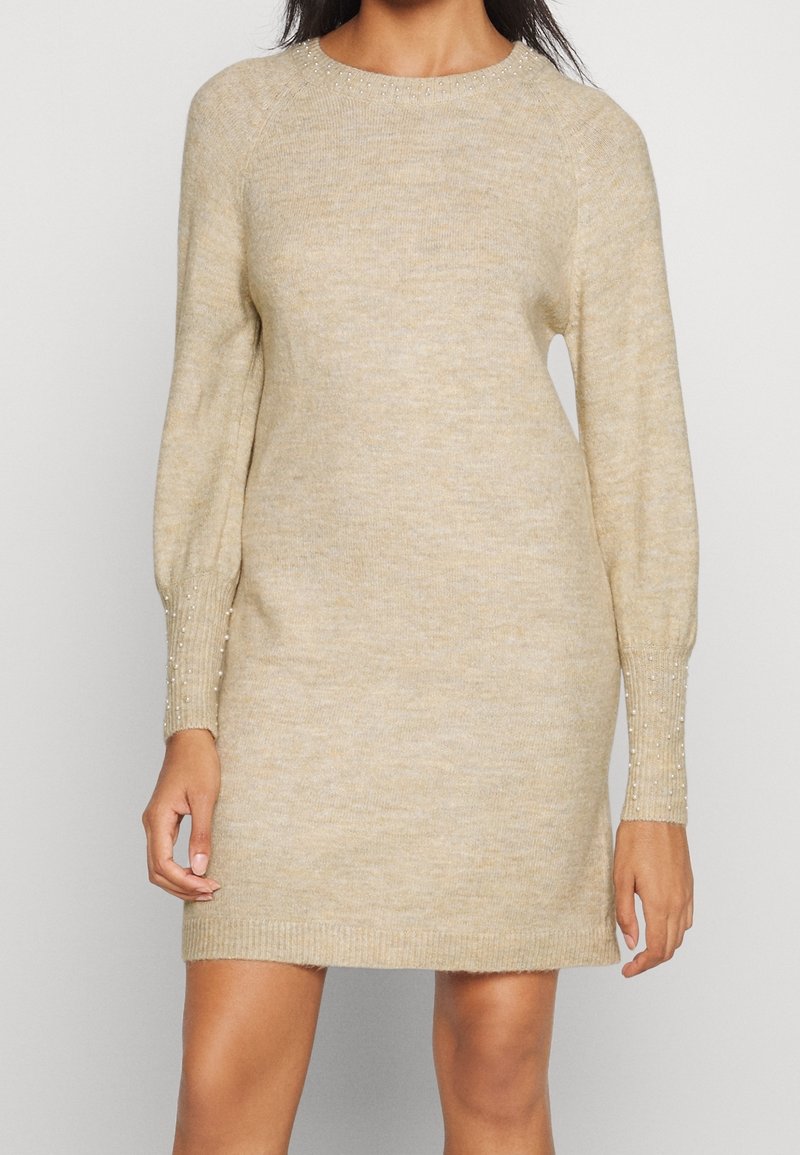 Robe-pull beige en maille avec manches raglan, ornée d'accents perlés sur les poignets, ourlet côtelé et texture lisse.