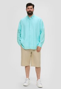 Lichtblauw linnen overhemd met knopen en lange mouwen, beige shorts en witte sneakers. Soepele textuur, ontspannen pasvorm en casual stijl.