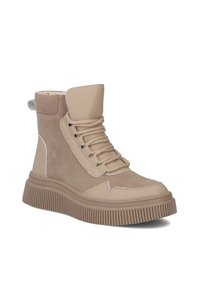 Beżowe sneakersy za kostkę z mieszanką gładkich i zamszowych tekstur, grubej gumowej podeszwy i wyraźnych sznurówek. Szczegółowe przeszycia podkreślają projekt.